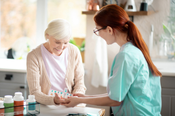 
A female care worker giving medication to an elderly woman