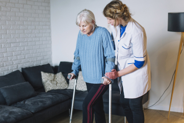 A female care worker helping an elderly woman with a walking frame